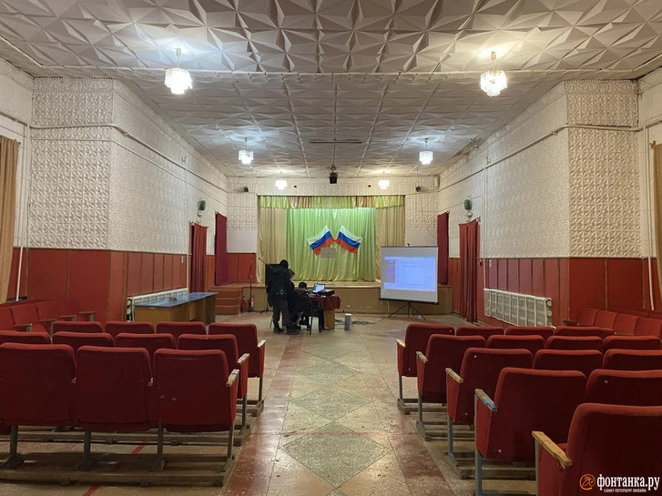 Drinnen steht ein Tisch mit einer bordeauxroten Tischdecke, daran sitzen eine Lehrerin und zwei Schüler. Sie proben für den 9. Mai / Foto © Alina Ampelonskaja