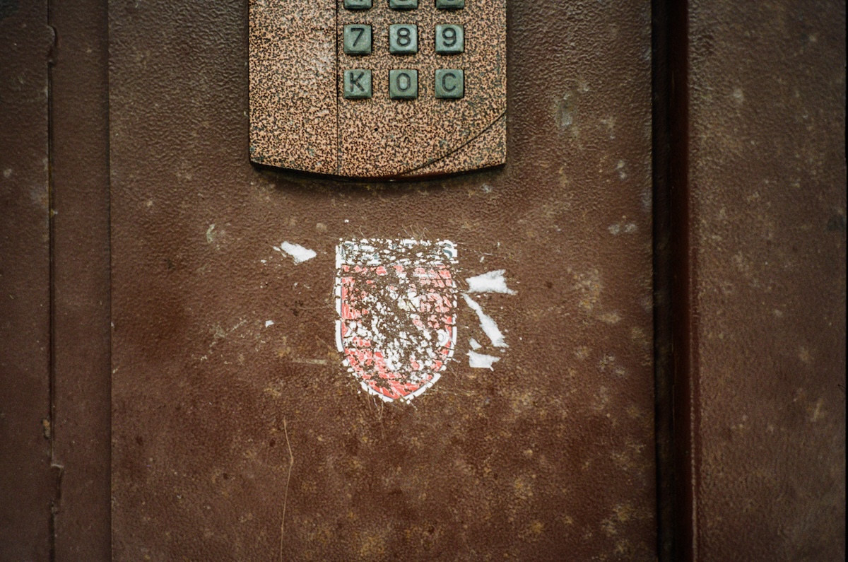 Abgekratzter Pahonja-Sticker, dem Staatswappen von Belarus von 1991—1995, an der Haustür eines Wohnhauses. Die Darstellung dieses Wappens wird in Belarus mit hohen Geld- oder Ordnungshaftstrafen geahndet. Kommunale Behörden entfernen jegliche in Zusammenhang mit dem Protest stehenden Abbildungen oder Aufschriften, Februar 2023 / Foto © privat 