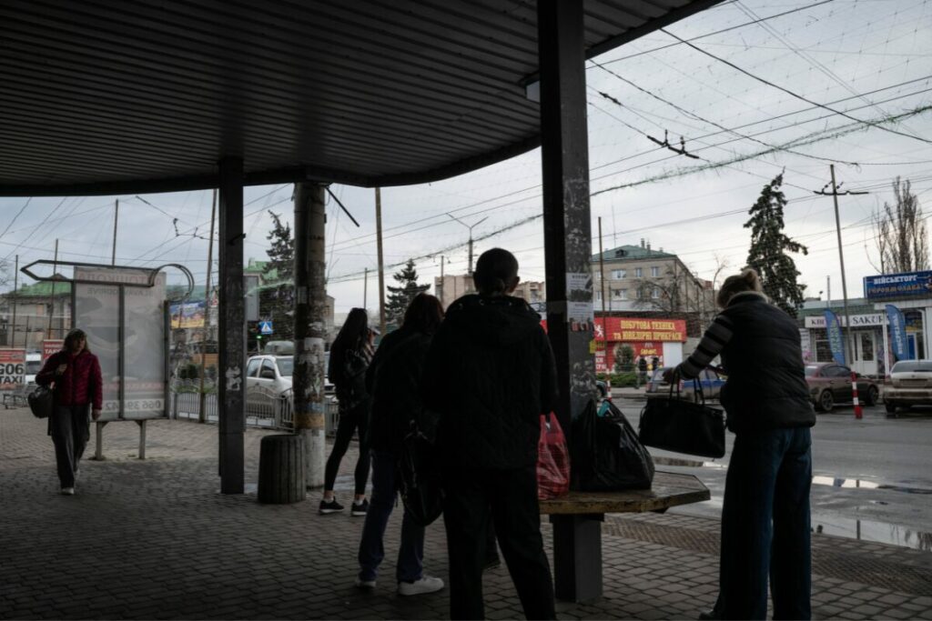 Slowjansk (Oblast Donezk) im März 2026: Menschen warten auf den Bus unter Anti-Drohnen-Netzen. In diesem Jahr steigen monatlich die Zahlen ziviler Kriegsopfer durch russische Luftangriffe, besonders im Osten der Ukraine. Die ukrainische Demografie steht durch Russlands Krieg extrem unter Druck. / Foto © Maciek Musial/Anadolu Agency/Imago